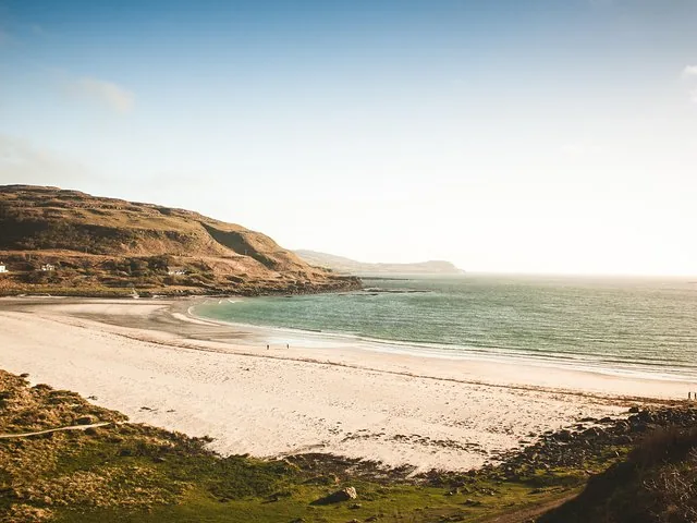 Ein breiter Sandstrand an einer ruhigen blauen Bucht unter strahlendem Himmel