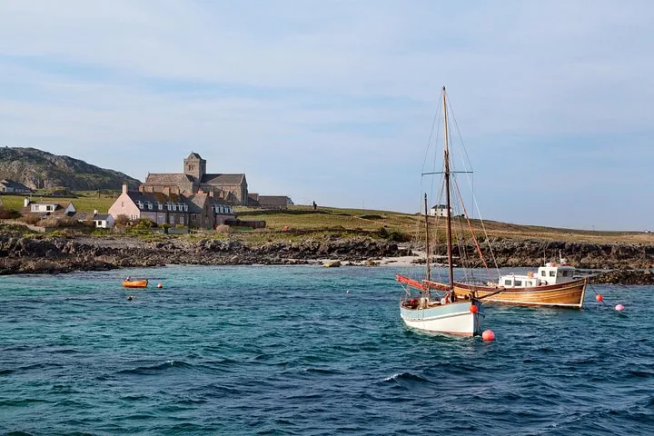 Boote, die vor einer grasbewachsenen Küste mit einem großen Steingebäude segeln