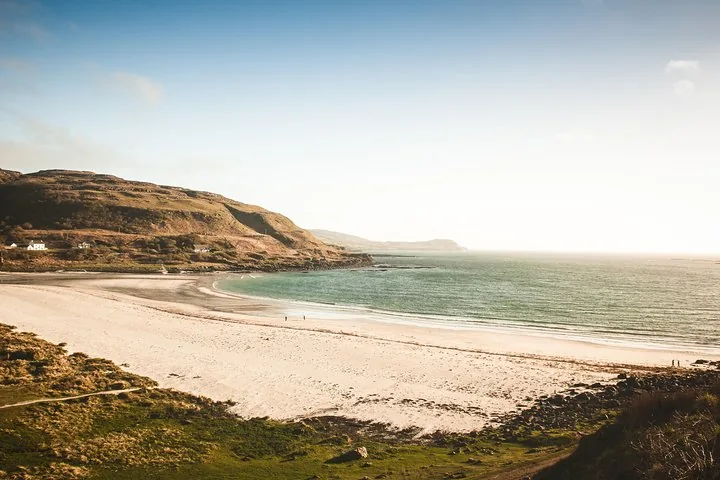 Ein breiter Sandstrand an einer ruhigen blauen Bucht unter strahlendem Himmel