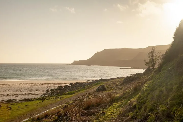 Ein Küstenweg entlang eines Strandes, der bei Sonnenuntergang zu fernen Hügeln führt