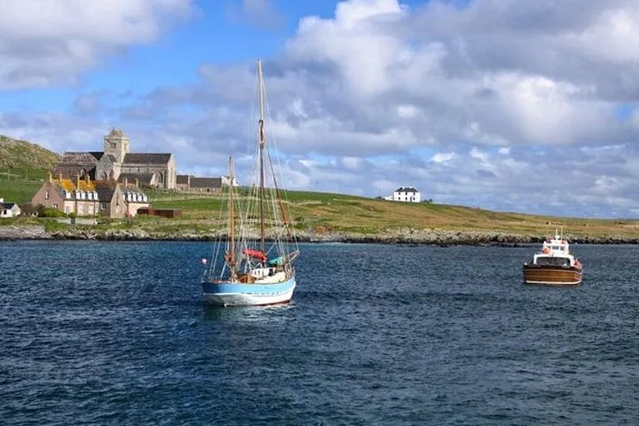 Boote, die vor einer grasbewachsenen Küste mit einem großen Steingebäude segeln